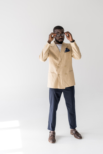 schöner stylischer junger afrikanisch-amerikanischer Mann mit Brille und Blick auf die Kamera auf grau - Foto, Bild