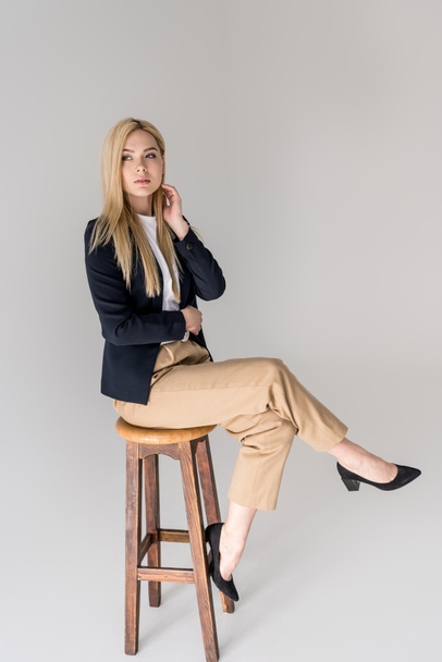 full length view of beautiful stylish blonde girl sitting on stool isolated on grey - Foto, Imagen