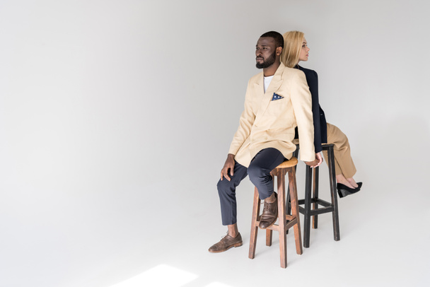 vista de alto ângulo de moda jovem casal multiétnico sentado de volta para trás no cinza
 - Foto, Imagem