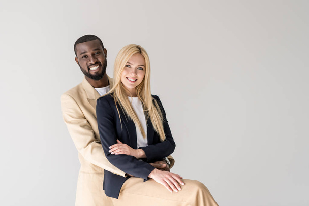 happy young multiethnic couple embracing and smiling at camera isolated on grey - Foto, immagini