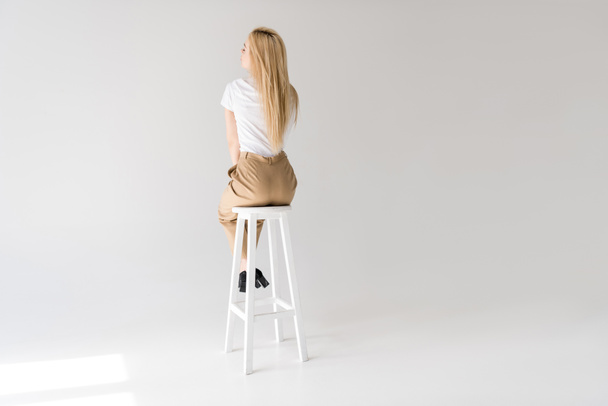 back view of stylish blonde woman sitting on stool on grey - Foto, afbeelding
