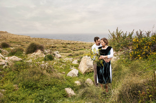 τρυφερό ζευγάρι που ντυμένος με ρετρό vintage ρούχα στέκεται αγκαλιάζουν στοργικά με φόντο Βροντερό τοπίο - Φωτογραφία, εικόνα