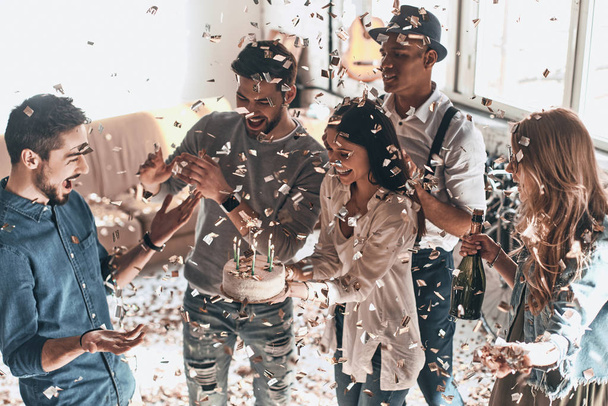 happy surprised man celebrating birthday with friends and cake in modern apartment with confetti - Foto, Bild