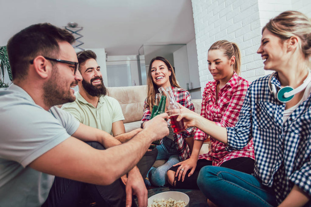 Група щасливих молодих друзів розважаються і п'ють пиво в домашньому інтер'єрі
 - Фото, зображення