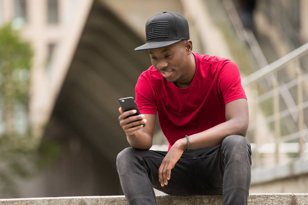 Молодой человек в розовой футболке использует приложение для смартфонов на городской улице
 - Фото, изображение