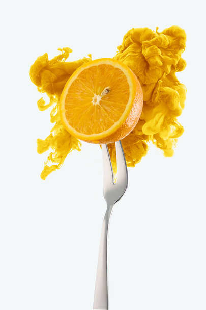 half of orange on fork and yellow ink isolated on white - 写真・画像