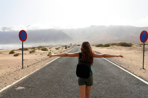 Женщина беззаботный турист наслаждается пейзажем посреди пустынной асфальтовой дороги. Ощущения свободные, глядя на захватывающий вид с пустой улицы в Льяроте, Испания
 - Фото, изображение