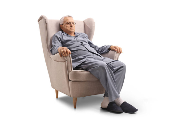 Grumpy old man in pajamas seated in an armchair isolated on white background - Photo, image