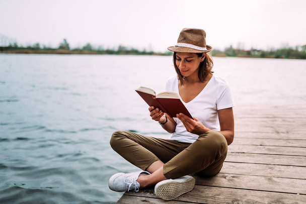 Smiling young woman reading book near water - Photo, image