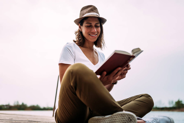 笑顔の若い女性は、水の近くの本を読んで - 写真・画像