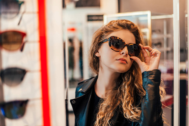 young woman choosing new sunglasses in optician store - Foto, afbeelding