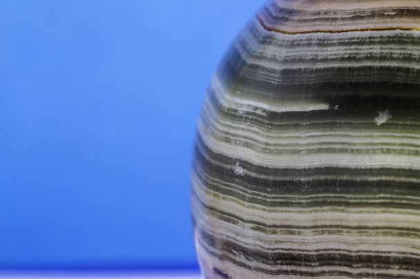 Macro photo texture de pierre d'onyx polie sur fond bleu. Photo pour le site sur la géologie, pierres, bijoux, travaux manuels, textures, art, astronomie
. - Photo, image