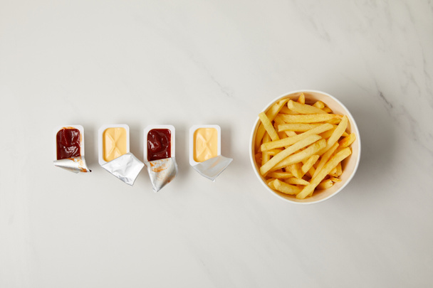 top view of french fries in bowl with containers of sauces in row on white - Photo, Image