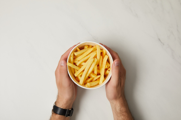cropped shot of man holding bowl of french fries on white - Foto, Bild