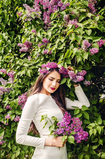 Joven modelo de moda con flores lila en la mano en el parque
  - Foto, Imagen