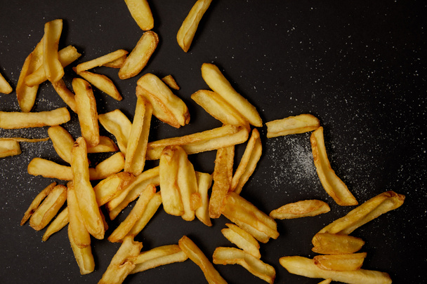 top view of delicious french fries spilled with salt on black - Photo, image