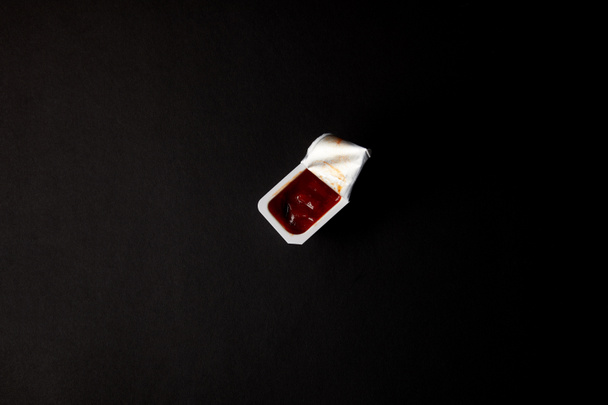 top view of plastic container with ketchup isolated on black - Φωτογραφία, εικόνα