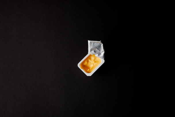 top view of plastic container with cheese sauce isolated on black - Foto, afbeelding