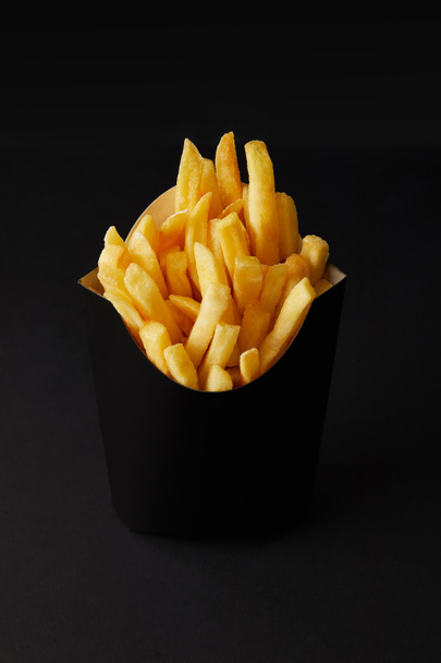 close-up shot of black box of tasty french fries isolated on black isolated on black - Фото, изображение