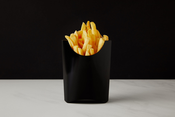 doos van Franse frietjes op witte marmeren oppervlak geïsoleerd op zwart - Foto, afbeelding