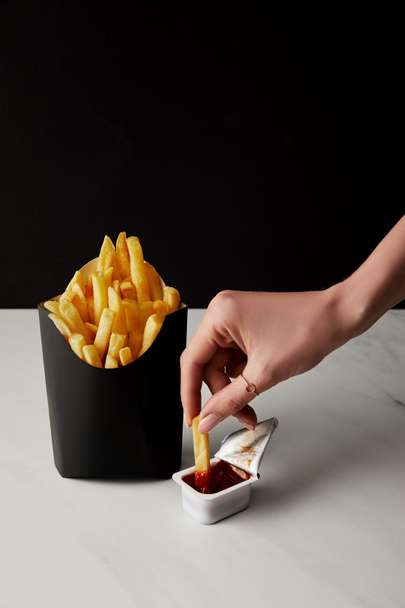 abgeschnittene Aufnahme einer Frau, die Frittiertes in Ketchup gießt, isoliert auf schwarz - Foto, Bild