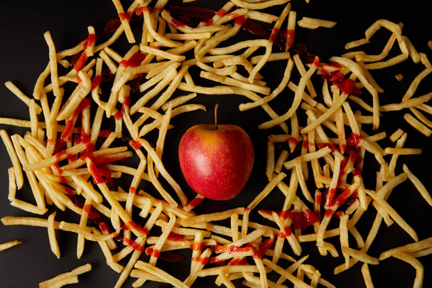 top view of red apple surrounded with french fries poured with ketchup isolated on black - Photo, Image