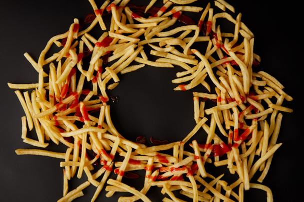 top view of french fries in shape of circle poured with ketchup isolated on black - 写真・画像