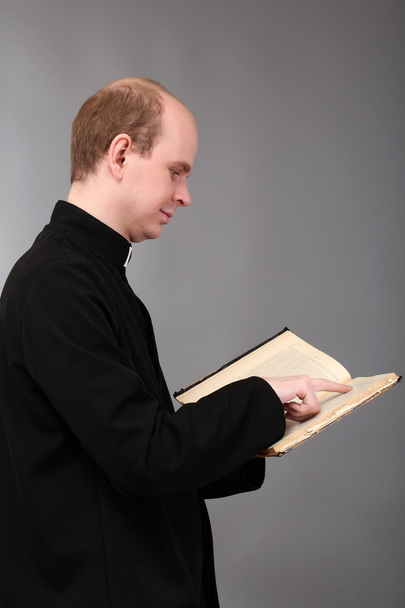 junger Pastor mit Bibel, auf grauem Hintergrund - Foto, Bild