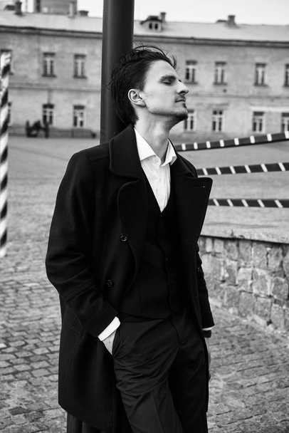 Fekete-fehér fénykép, elegáns, csinos fiatalember pózol az utcán - Fotó, kép