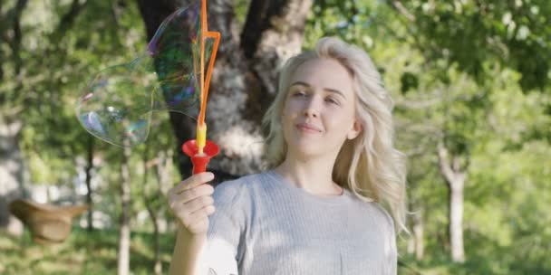 Portrait of happy young blonde woman play with soup bubbles in summer  - Felvétel, videó