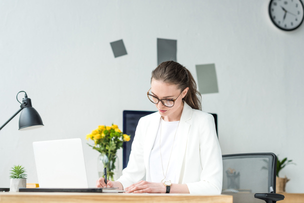 portrait d'une femme d'affaires concentrée faisant de la paperasse sur le lieu de travail avec un ordinateur portable au bureau
 - Photo, image
