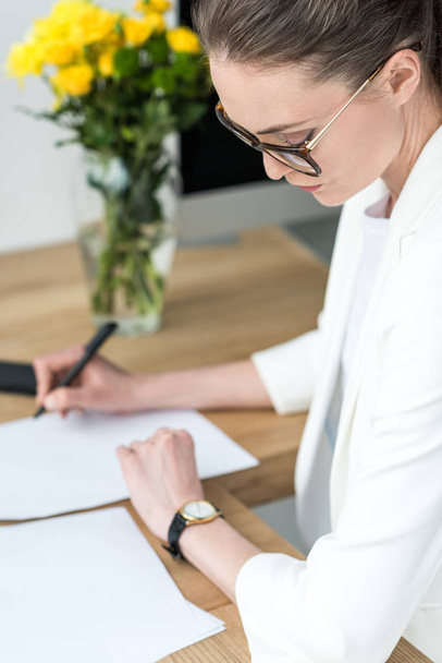 selektiver Fokus der Geschäftsfrau, die Zeit kontrolliert, während sie Papierkram am Arbeitsplatz im Büro erledigt - Foto, Bild