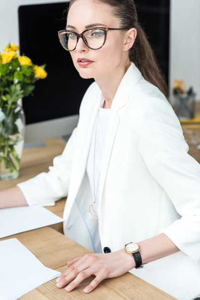 portrait of pensive businesswoman in eyeglasses at workplace in office - Foto, imagen