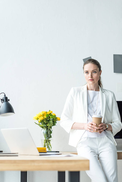 portrait of pensive businesswoman with coffee to go in office - Фото, изображение