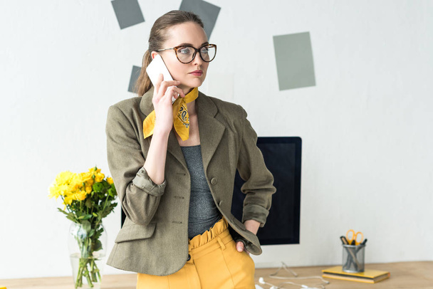 beautiful stylish businesswoman talking by smartphone and looking away in office - Photo, Image