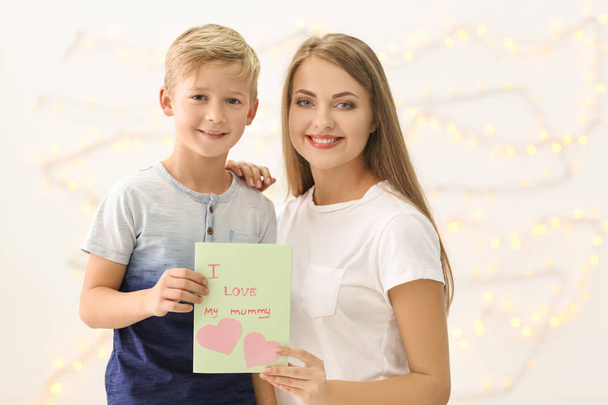 Young woman with her little son and Mother's Day greeting card on blurred background - Photo, image