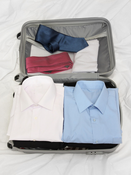 Open grey suitcase with clothing on bed - Foto, Imagem