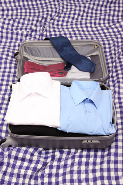 Open grey suitcase with clothing on plaid - Foto, Imagen