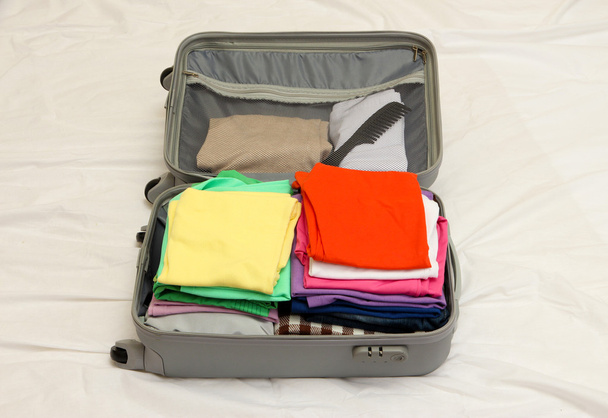 Open grey suitcase with clothing on bed - Foto, Imagen