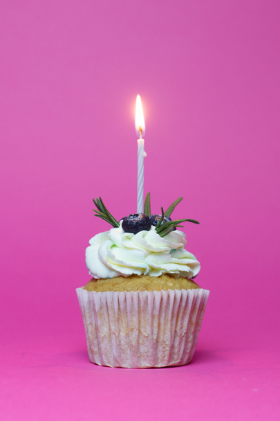 праздничный кекс с одной горящей свечой на розовом фоне
 - Фото, изображение