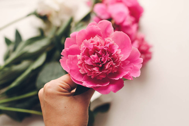 bovenaanzicht van hand hebt mooie roze pioen bloem op rustieke witte houten achtergrond - Foto, afbeelding