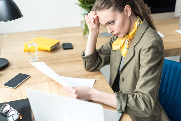 высокий угол зрения сфокусированной деловой женщины, держащей бумагу на рабочем месте
 - Фото, изображение
