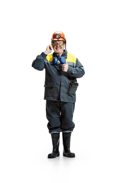 The studio shot of happy senior bearded male miner standing at the camera with smartphone on a white background. - Foto, Imagen