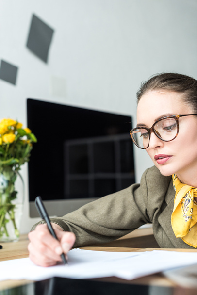 beautiful businesswoman in eyeglasses taking notes at workplace - Foto, afbeelding