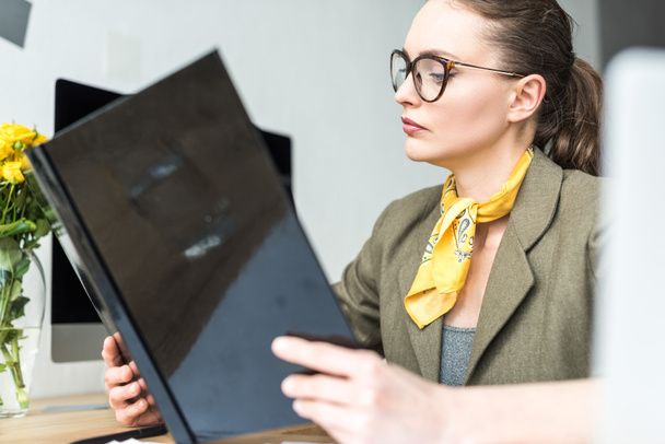 stylish businesswoman in eyeglasses holding folder at workplace - Fotó, kép