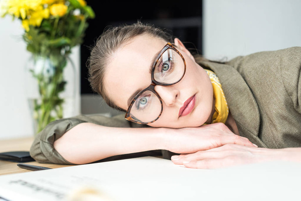 portrait of beautiful businesswoman in eyeglasses looking at camera while leaning at table in office - Photo, Image