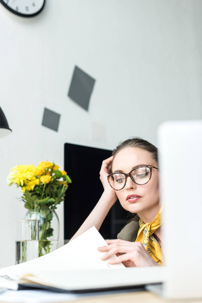 enfoque selectivo de mujer de negocios con estilo en gafas de lectura revista de negocios en la oficina
  - Foto, Imagen