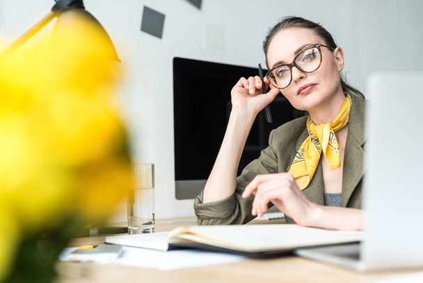 enfoque selectivo de hermosa mujer de negocios con estilo pensativo en gafas sentado en el lugar de trabajo
 - Foto, Imagen