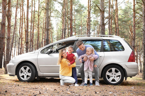 Jovem casal com seus filhos perto de carro na floresta de pinheiros
 - Foto, Imagem
