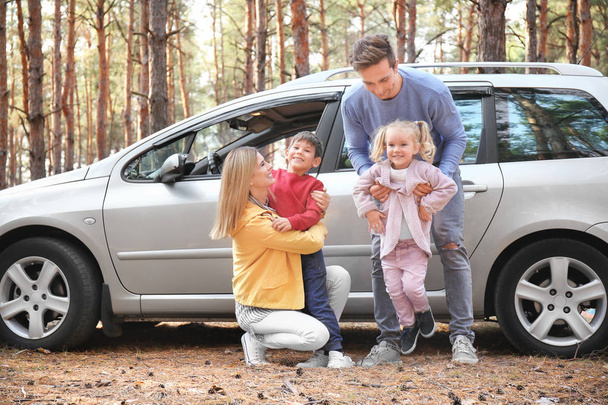 Молода пара зі своїми маленькими дітьми біля машини в сосновому лісі
 - Фото, зображення